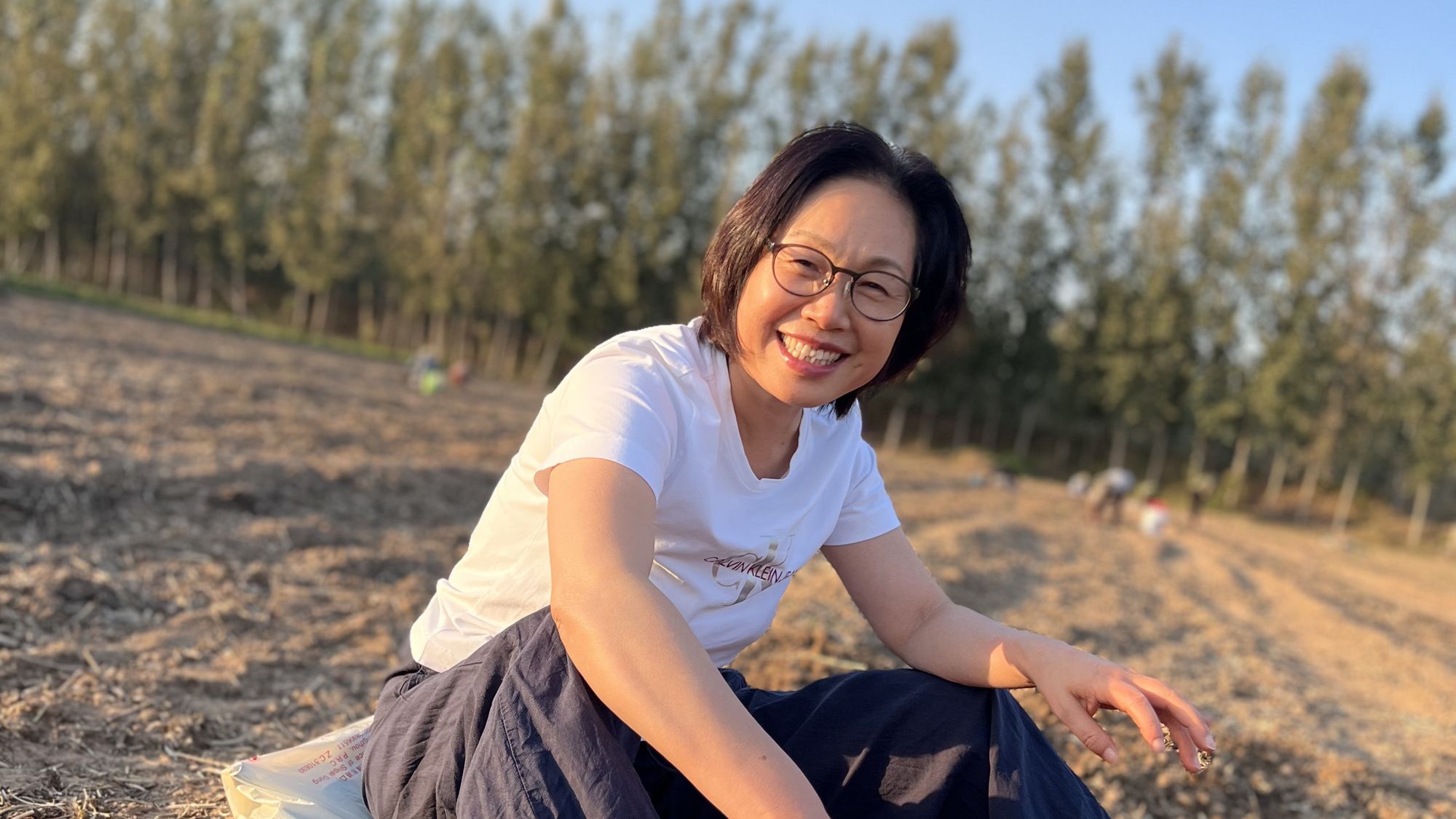 夕阳下坐在田里的人，回头微笑，身后是杨树林和风车