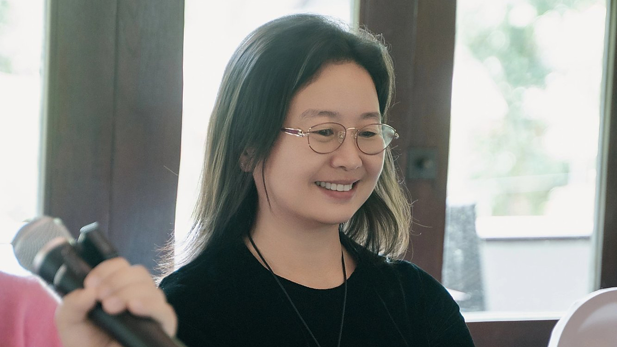 人像：窗边，戴眼镜、穿黑衣的长发女士低头微笑